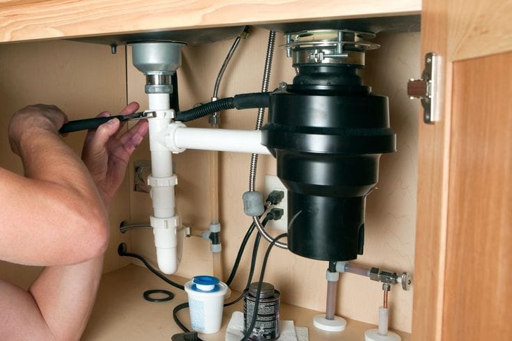 Plumber installing a garbage disposal beneath a kitchen sink in Lehigh Acres