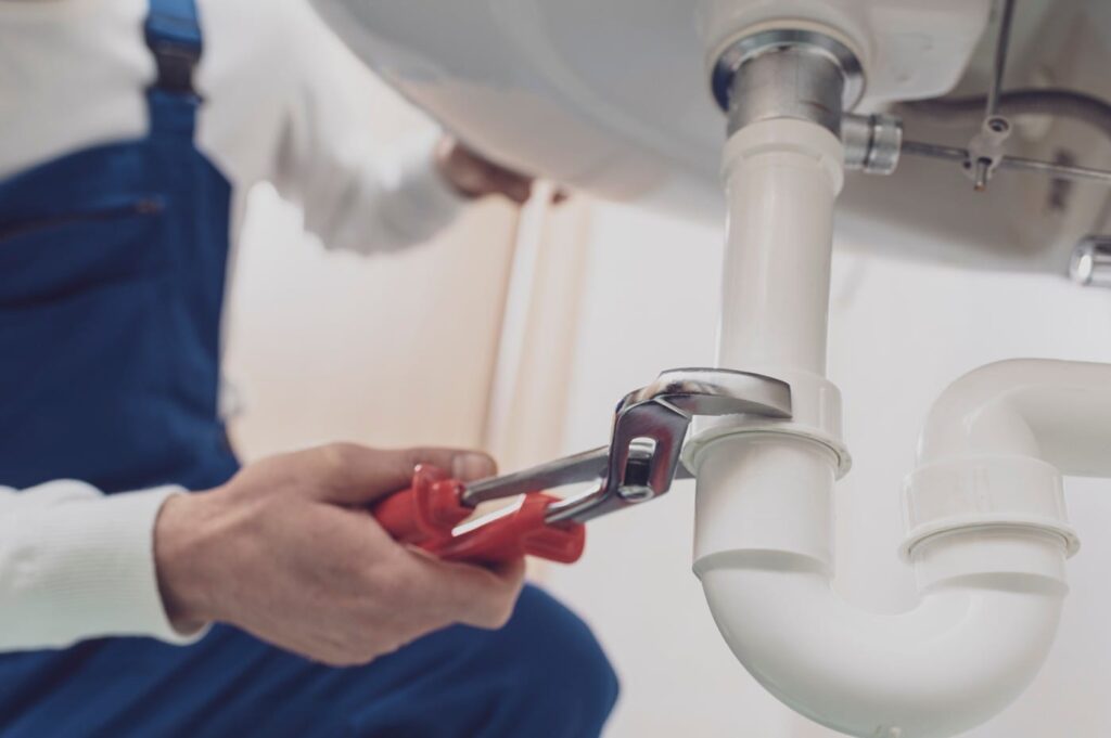 Plumber repairing a white drain pipe beneath a sink in Lehigh Acres